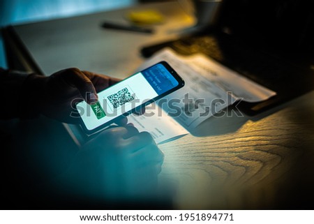 Close up of an African American male hand holding mobile phone with QR payment app on screen, at a desk with a laptop and a bill Royalty-Free Stock Photo #1951894771