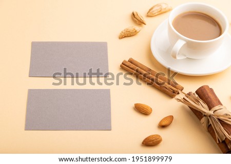 Composition of gray paper business cards, almonds, cinnamon and cup of coffee. mockup on orange background. Blank, side view, still life, copy space.