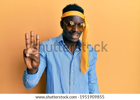 Handsome black man drunk wearing tie over head and sunglasses showing and pointing up with fingers number three while smiling confident and happy. 