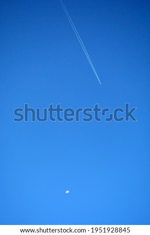 The moon and a flying plane against the background of a bright blue sky