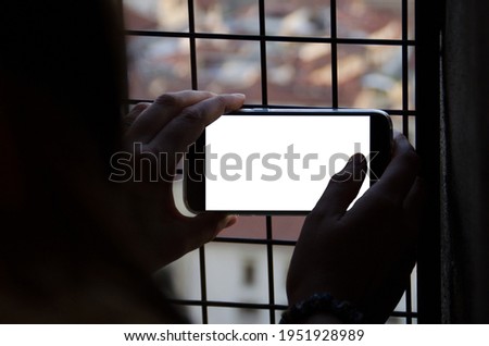 hands of a woman holding the phone to take a picture in a window with a grill