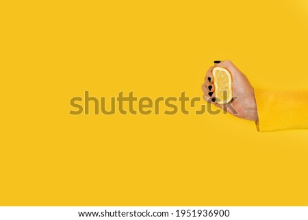 Woman squeezing a half lemon on a yellow background with copy space Royalty-Free Stock Photo #1951936900