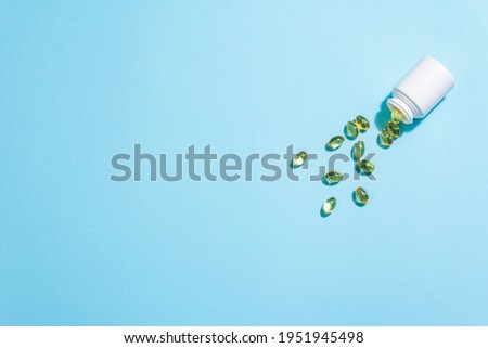 Omega-3 tablets scattered from the bottle on a blue matte background. Healthy life concept, prevention of various diseases. Trendy hard light, dark shadow, flat lay, mockup, template, top view