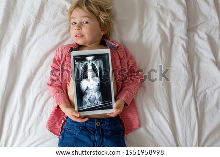 Toddler child, blond boy, holding x-ray picture on tablet of child body with swallowed magnet showing, child swallow dangerous object