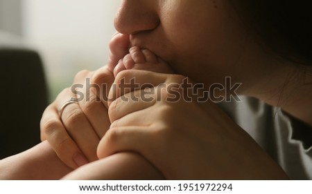 Authentic young mother gently kissing little feet of newborn baby child. Tender loving caring mum with baby's leg.
