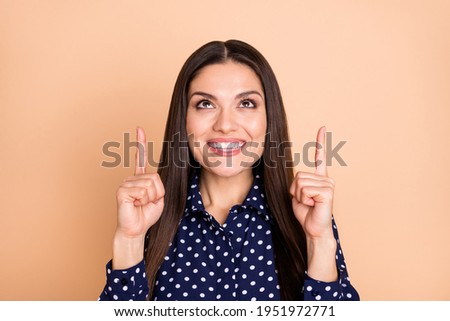 Photo of attractive positive person look indicate fingers up empty space promotion isolated on beige color background