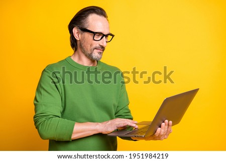 Photo of smart guy hold laptop work look screen wear spectacles green pullover isolated yellow color background