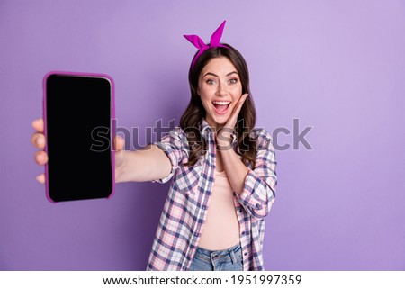 Photo portrait of happy female blogger touching cheek showing smartphone screen isolated on bright violet color background