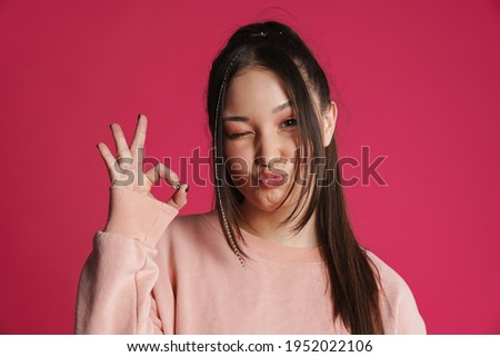 Asian brunette woman winking and gesturing ok sign isolated over purple wall