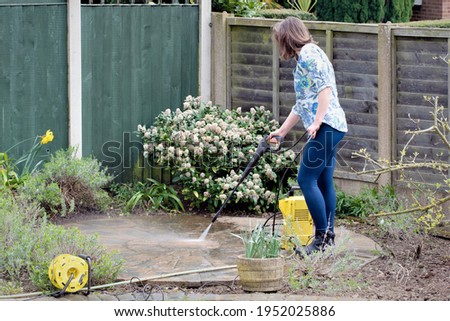 An energetic woman uses a power washer to transform a black coloured stone circle to its original red brick colour, by removing engrained dirt from the surface.