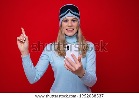 Portrait of a young woman in a sweater and ski goggles with a phone