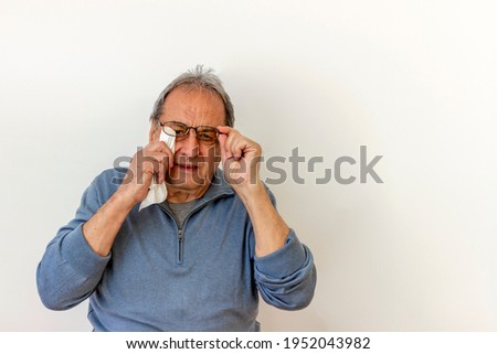 Photo of a old man with soft white cloth cleaning the lens of a pair of spectacles. Mature grey haired man cleaning his eyeglasses isolated on the white background. Vision and people concept.