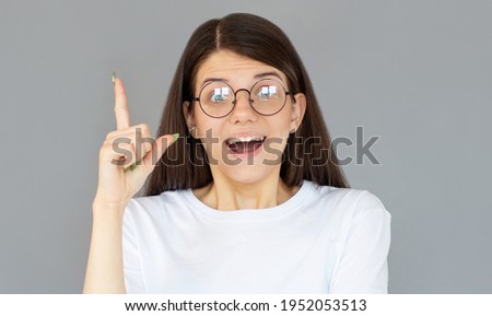 Photo of energetic nice smiling lady wearing white t-shirt isolated on gray background pointing her finger in eureka sign, having great innovative idea, understanding or solution she has just got.