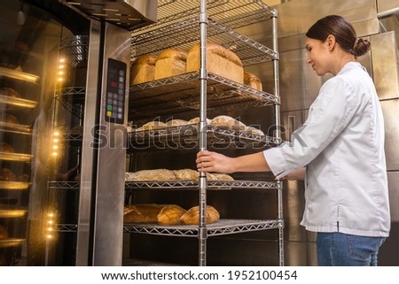 Woman in uniform standing near oven in bakery