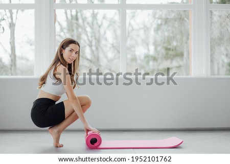Time for meditation, fitness session, well-being concept. Girl wearing grey sporty pants rolling fitness mat before, after class in yoga studio club or at home on wooden floor. Hands and legs close up Royalty-Free Stock Photo #1952101762