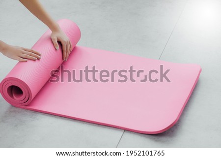 Time for meditation, fitness session, well-being concept. Girl wearing grey sporty pants rolling fitness mat before, after class in yoga studio club or at home on wooden floor. Hands and legs close up Royalty-Free Stock Photo #1952101765
