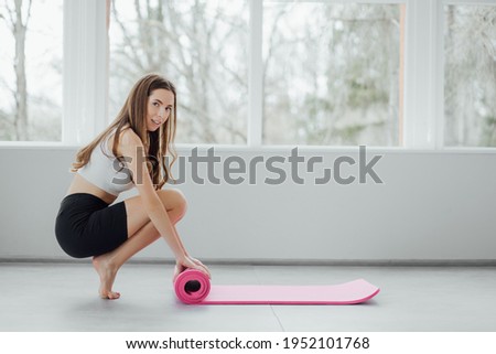 Time for meditation, fitness session, well-being concept. Girl wearing grey sporty pants rolling fitness mat before, after class in yoga studio club or at home on wooden floor. Hands and legs close up