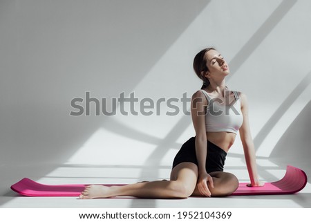 Fit adult woman resting in gym after a hard workout. Long haired caucasian coach sitting on yoga mat. Fitness concept.