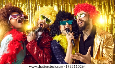 Male and female music show band with mikes performing on golden stage. Happy people dressed in funny fancy costumes having fun singing at New Year, Christmas, birthday or Halloween karaoke disco party