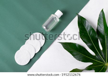 Make-up remover in small bottle and cotton discs on the green and white background. Cleansing skincare product Royalty-Free Stock Photo #1952112676