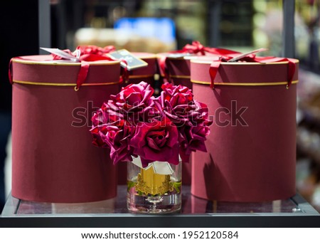 Decorative flowers in vase. beautiful flowers in pots. Transparent glass vase and artificial fake roses flowers on a red gift boxes background. Valentine's day, Womens Day gifts. Selective focus