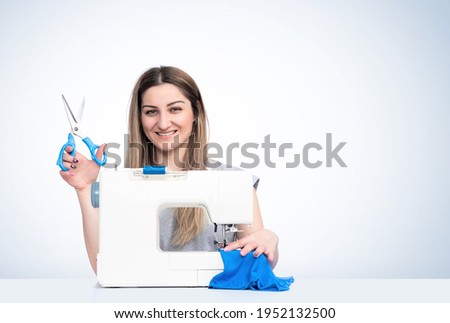 Young happy girl with scissors in her hands works at the sewing machine, on light blue background