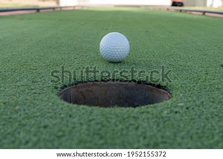 Minature or mini golf hole close up with ball in center on green artificial turf outdoors.