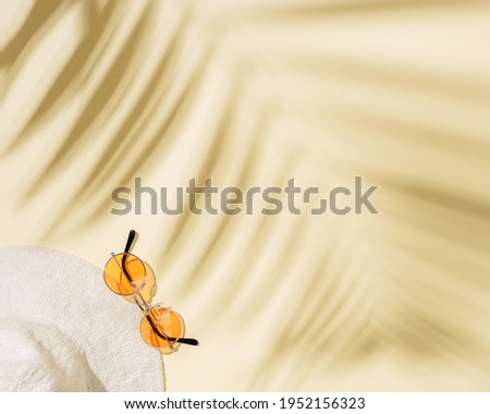 Summer flat lay with wide-brimmed hat, colored sunglasses on sandy color background with shadows of palm leaves and copy space. Concept of summer hot day on beach.