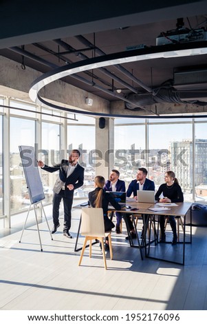 The boss stands near the board with graphs, demonstrates statistics, various personnel attending the training, introduces the new products of the company, reports on the results of work for partners. Royalty-Free Stock Photo #1952176096