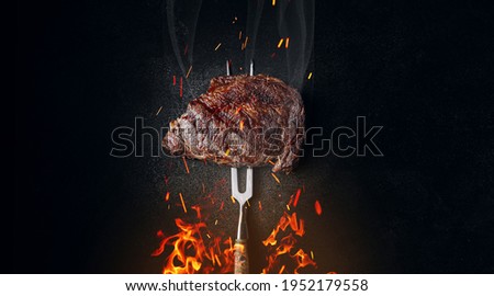 medium rare steak on an iron fork on a dark background. from below, fire and sparks. meat and fire. Royalty-Free Stock Photo #1952179558