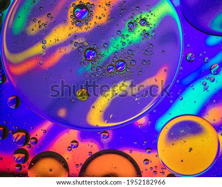 Photography with an abstract theme, with drops of oil mixing with water inside a glass container. that is on top of a tablet with psychedelic drawings.
