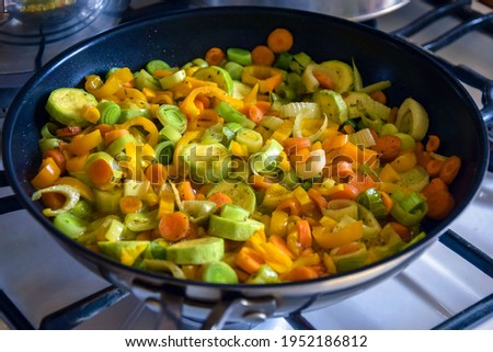 Vegetable saute in frying pan on gas stove. Process of cooking stewed vegetables at home. Ingredients leek, carrot, zucchini, bell pepper. Close-up. Selective focus. Royalty-Free Stock Photo #1952186812
