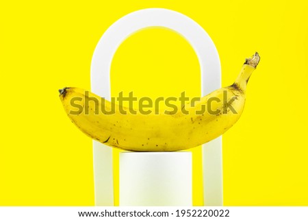 Aesthetic minimalism food photography. Banana on yellow background. Abstract scene with white geometrical forms. 