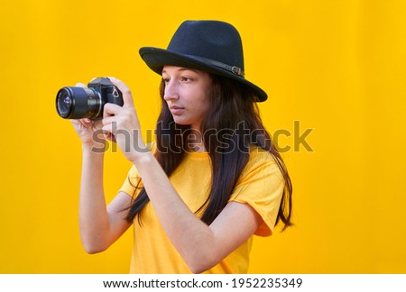 Young girl with hat taking a picture in right direction on yellow background