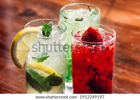 Summer refreshing drink with ice, strawberry lemonade and mojito cocktail in a tall glass, on a wooden background