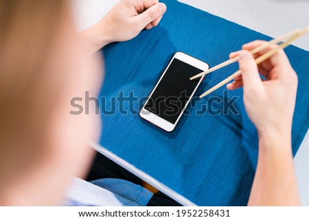 Mockup for ordering Japanese and oriental cuisine online: hand holding chopsticks and smartphone screen