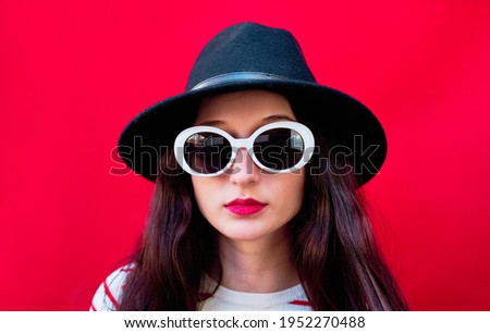 Close-up Portrait of a young girl with sunglasses and hat on red background