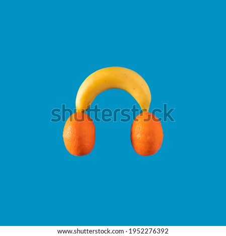 Colorful tropical summer background fruit.  Music toy made of banana and mandarins on blue background. Creative pop art design. Hipster headphones on orange and yellow colors. Minimal food concept.