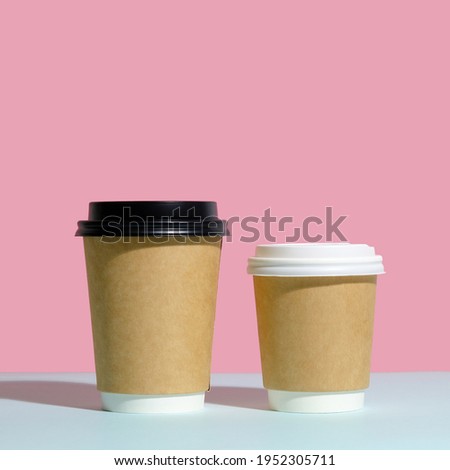 Two paper disposable coffee containers with lids on trendy pink and blue background. Takeaway coffee containers mockup.