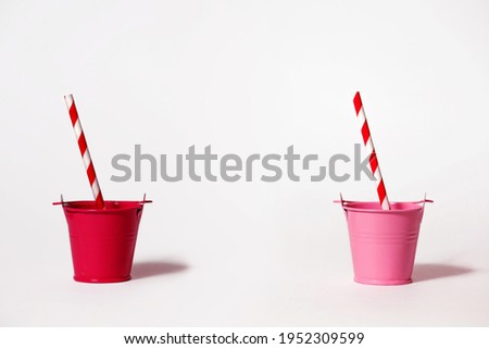 Two buckets on a white background with striped red and white straws. A red and pink bucket around the edges of the photo with free space for text in the center. Cool party or thirsty hot day concept