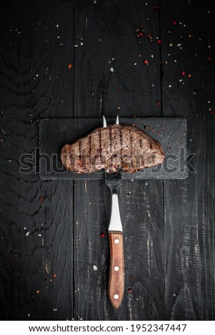 Steak on fork on dark wooden background. banner, menu recipe place for text, top view vertical image.