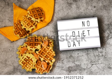 A lightbox with the text NO DIET DAY with Viennese waffles and yellow napkin on a concrete gray background. National Day without Diets.
