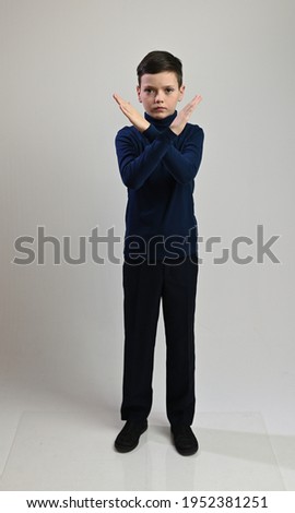 Teen boy in full growth in dark clothes on a white background shows stop