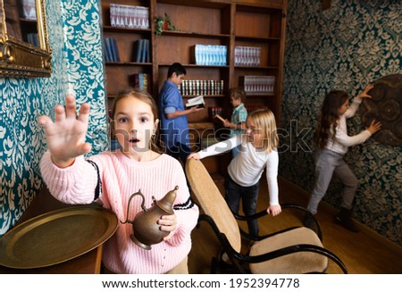 Interested tween girl trying to reach for some item in escape room stylized as old library, holding out her hand . Royalty-Free Stock Photo #1952394778