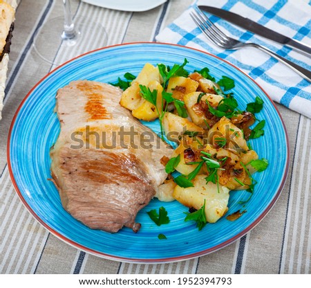 Delicious fried pork tenderloin with potatoes, served with greens on plate