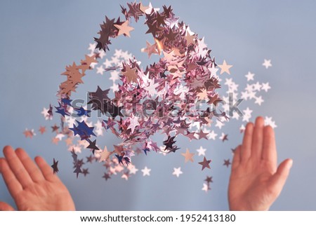 Woman hands toss pink glittering confetti on a blue background, Christmas and celebration concept.