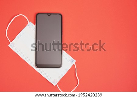 smartphone and face mask on a red background, necessary things for a modern person top view copy space