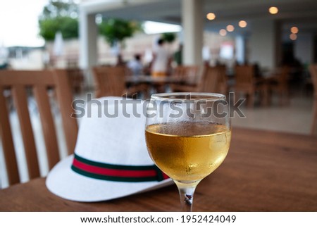 A glass of wine and white hat on table. Condensation on the glass of refreshing wine. Cool drink in open-air restaurant.