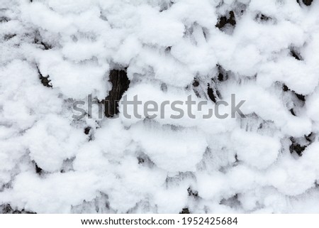 Whimsical snow patterns on snow-covered wooden fence. Snowy uneven crust on the wall as background