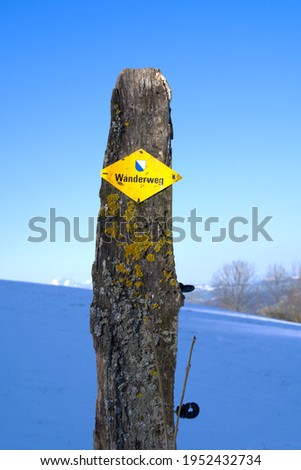 Wooden pole with yellow sign Wanderweg (German, translation ist hiking trail). Photo taken April 8th, 2021, Wernetshausen, Switzerland.